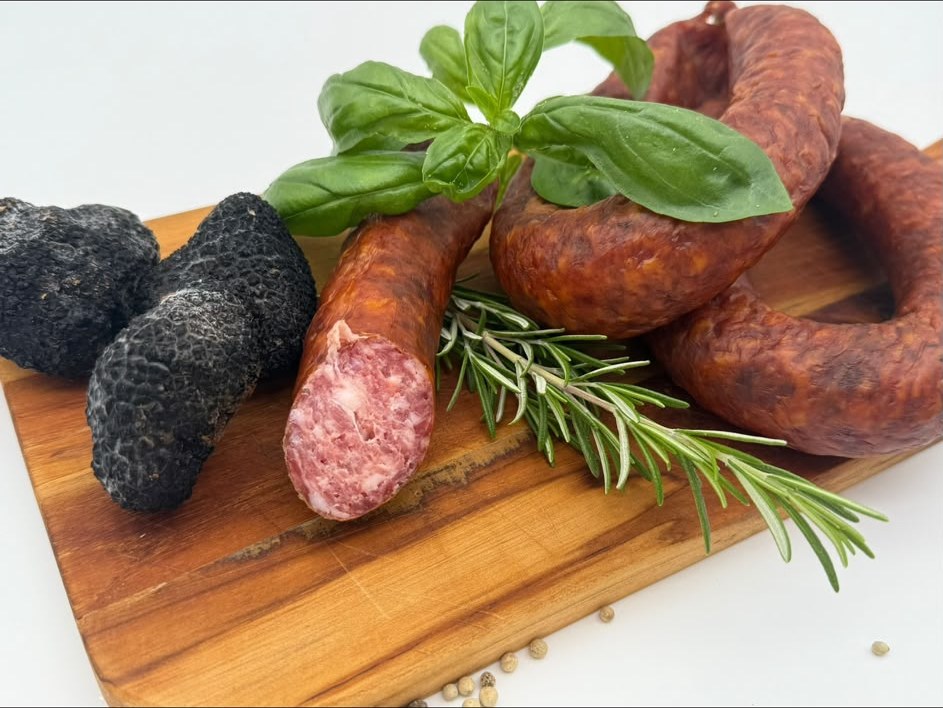 Angeschnittene Trüffel-Knackwurst mit frischen schwarzen Trüffeln auf einem Olivenholzbrett