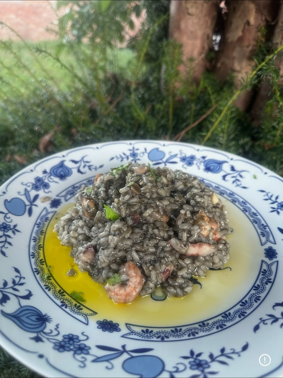 Zubereiteter Risotto Nero mit Garnelen und Meeresfrüchten, angerichtet auf einem Teller
