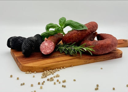 Trüffel-Knackwurst auf einem Olivenholzbrett mit frischen schwarzen Trüffeln und weißen Pfefferkörnern